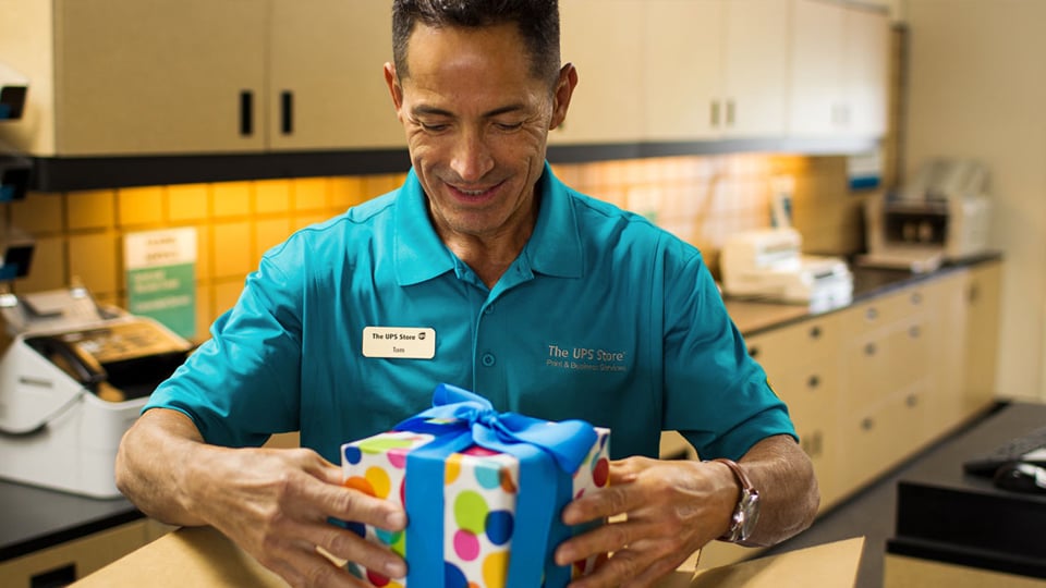 The UPS Store employee securely packing a wrapped gift tied with a satin bow