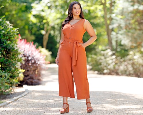 Woman is wearing a plus size orange sleeveless jumpsuit from Cato Fashions.