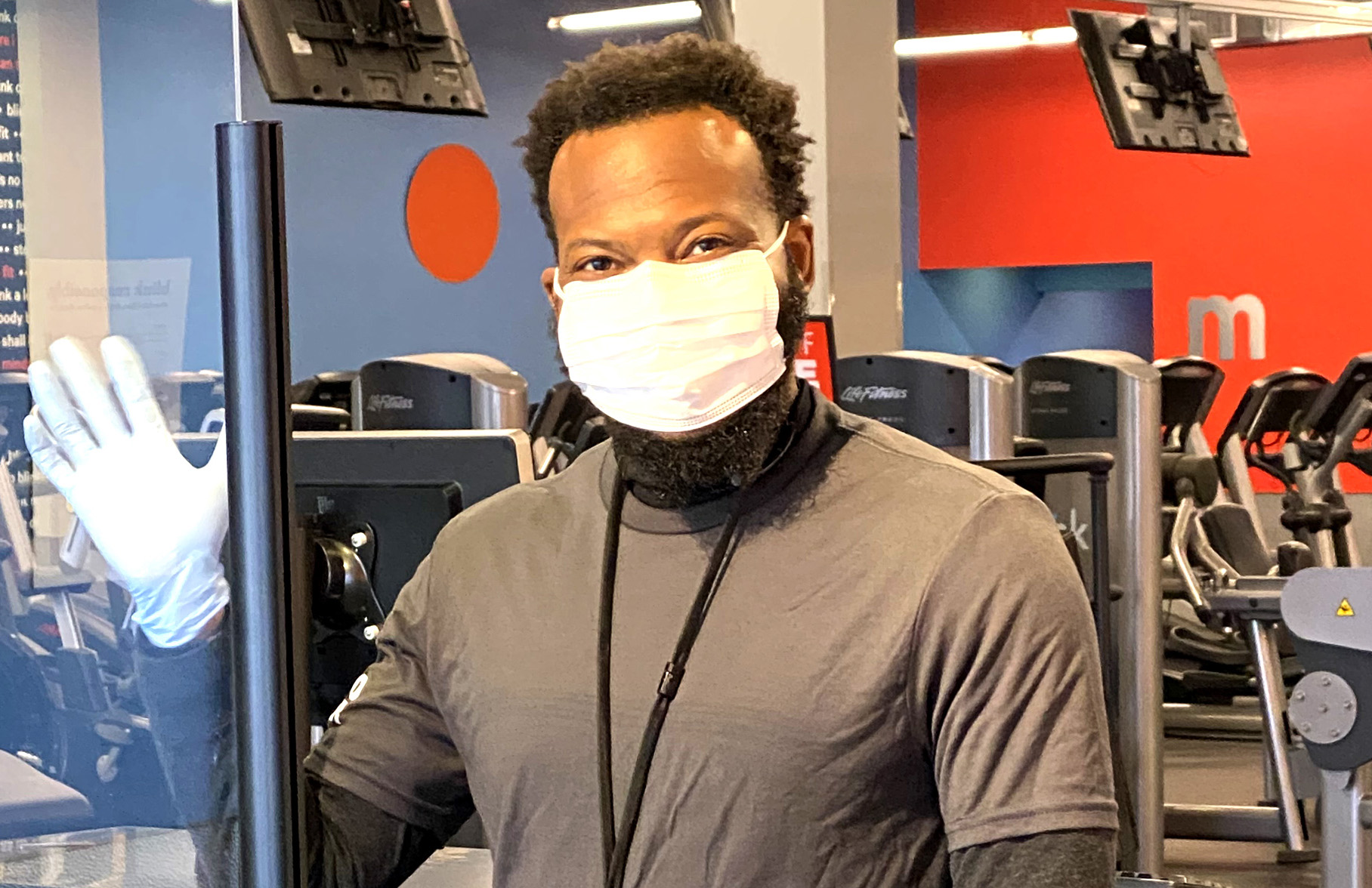 Blink Fitness Employee wearing a mask waving behind the front desk.