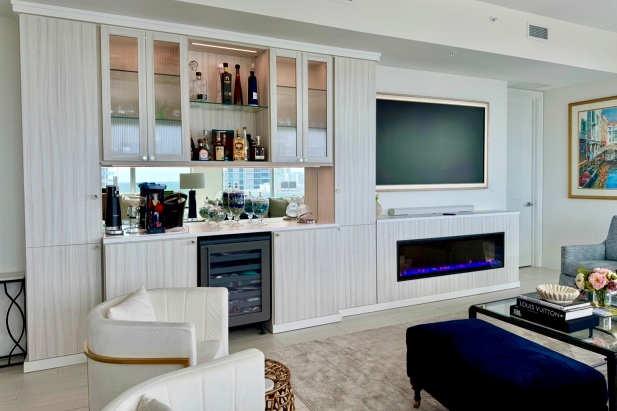 Fireplace & Cocktail Bar in Tuscan Moon & Dove with Reeded Glass Custom fireplace and cocktail bar in Tuscan Moon and Dove with shaker doors featuring reeded glass inserts, City Light glass knobs in satin brass by Schaub, glass shelving, and mirrored backing for a sophisticated, functional space.