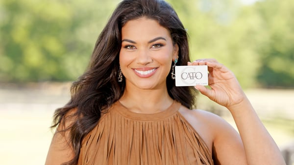 Woman is smiling and holding a Cato Fashions gift card.