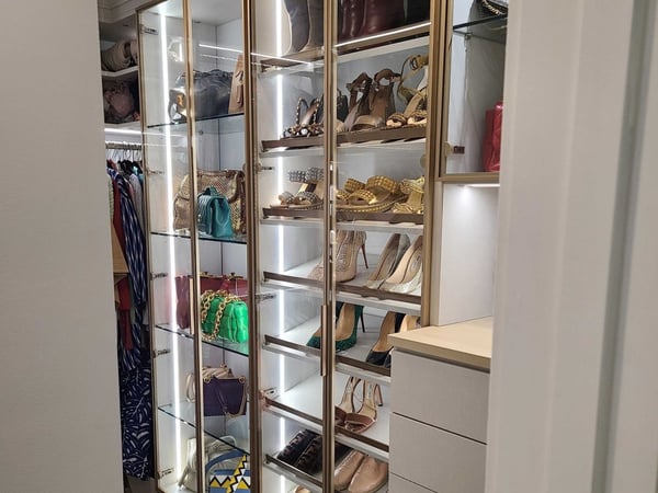 Boutique-inspired closet storage turns shoes and accessories into a curated display with floor-to-ceiling shelving, integrated lighting, and dedicated organization for every piece. Custom walk-in closet with illuminated floor-to-ceiling shoe shelving, glass-front storage, drawers, and organized accessories.