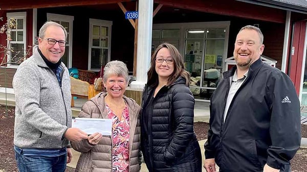 Four people standing next to each other. Two people are holding a check.