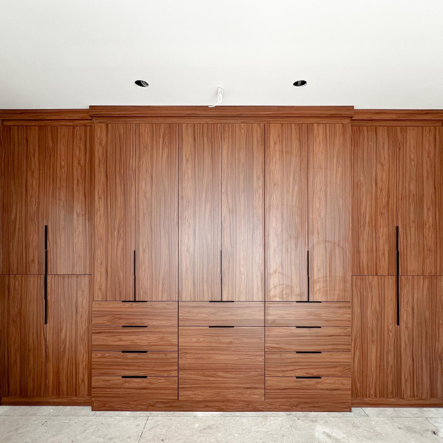 Sleek Bedroom Wardrobe Floor to ceiling wardrobe in a reddish brown finish and black hardware.
