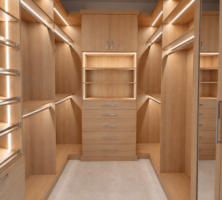 Custom Walk-In Closet with LED Lighting Luxury custom walk-in closet with natural wood cabinetry, illuminated shelving, spacious drawers, and organized hanging sections.