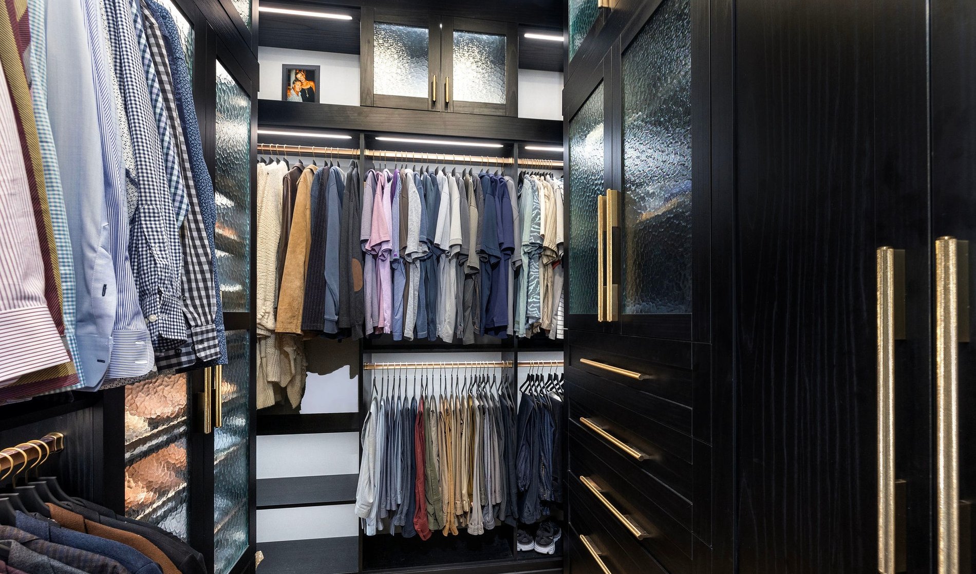 Walk-in Closet with Gold Accents | California Closets Memphis Masculine walk-in closet with shoe storage, custom lighting, and hanging space by California Closets Memphis, Tennessee.