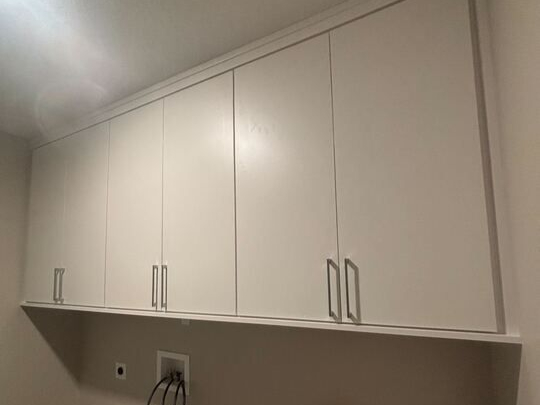 Sleek overhead cabinetry brings thoughtful storage and understated luxury to the laundry room, designed by California Closets Virginia Beach. Virginia Beach – Laundry room – Custom overhead cabinetry above utility sink and appliance space