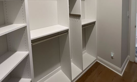 An airy, refined walk-in closet tailored for versatility and simplicity, offering ample storage for every lifestyle by California Closets Virginia Beach. Virginia Beach – Custom closet – White walk-in closet with open shelving, hanging rods, and modern design