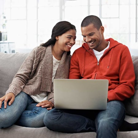 A couple smiles at each other as they apply online from their couch
