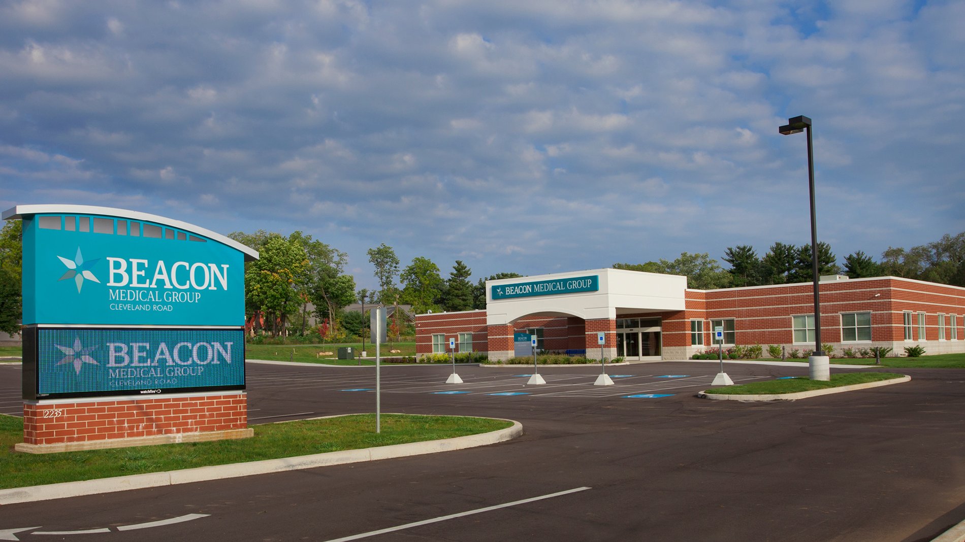A modern teal sign stands in front of the brick building Beacon Medical Group Cleveland Road.