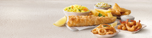 Fried fish, calamari, scampi, rice, coleslaw and ships arranged on a grey table