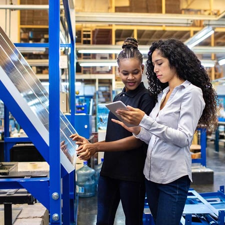 Two women looking at a tablet next to solar panels