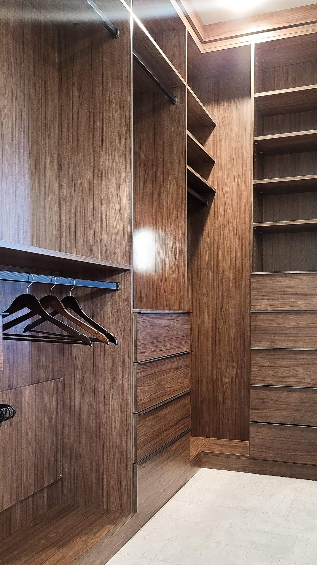 Dark and Moody Walk In Closet A floor to ceiling walk-in designed in a dark wood grain finish. Open shelving, double hanging, and drawers provides lots of storage options.
