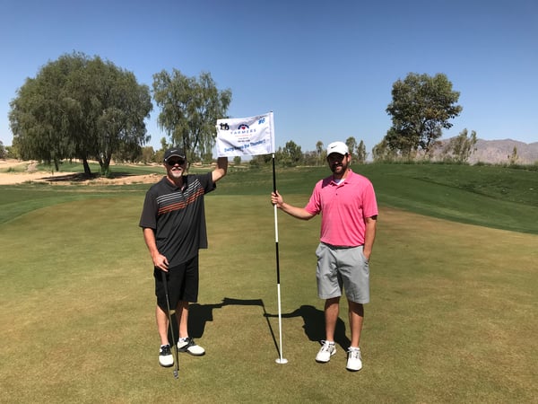two men holding a Farmers Flag on a golf course