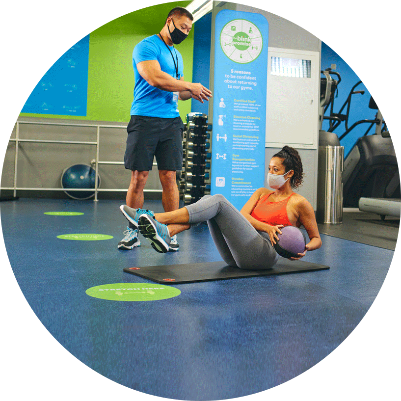 personal trainer coaching a client in the gym. The client is female and sitting on a mat doing ab exercises.