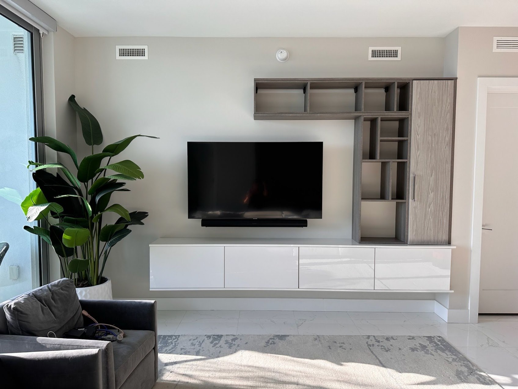 A minimalist media wall blends entertainment and storage with floating cabinetry, open display shelving, and a clean neutral palette designed to complement the surrounding living space. Modern custom media wall with floating white cabinetry, wall-mounted television, open shelving, and built-in storage.