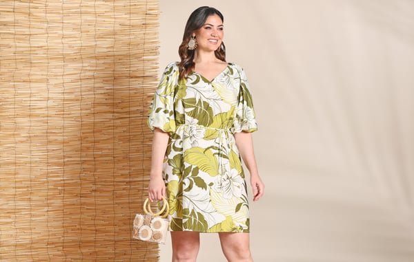 Woman is wearing a green plus size short dress and is holding a small purse.