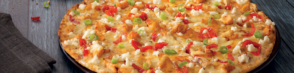 Pizza with feta, cheddar cheese, sweet bell peppers and spring onion on a plate on a grey wooden surface.