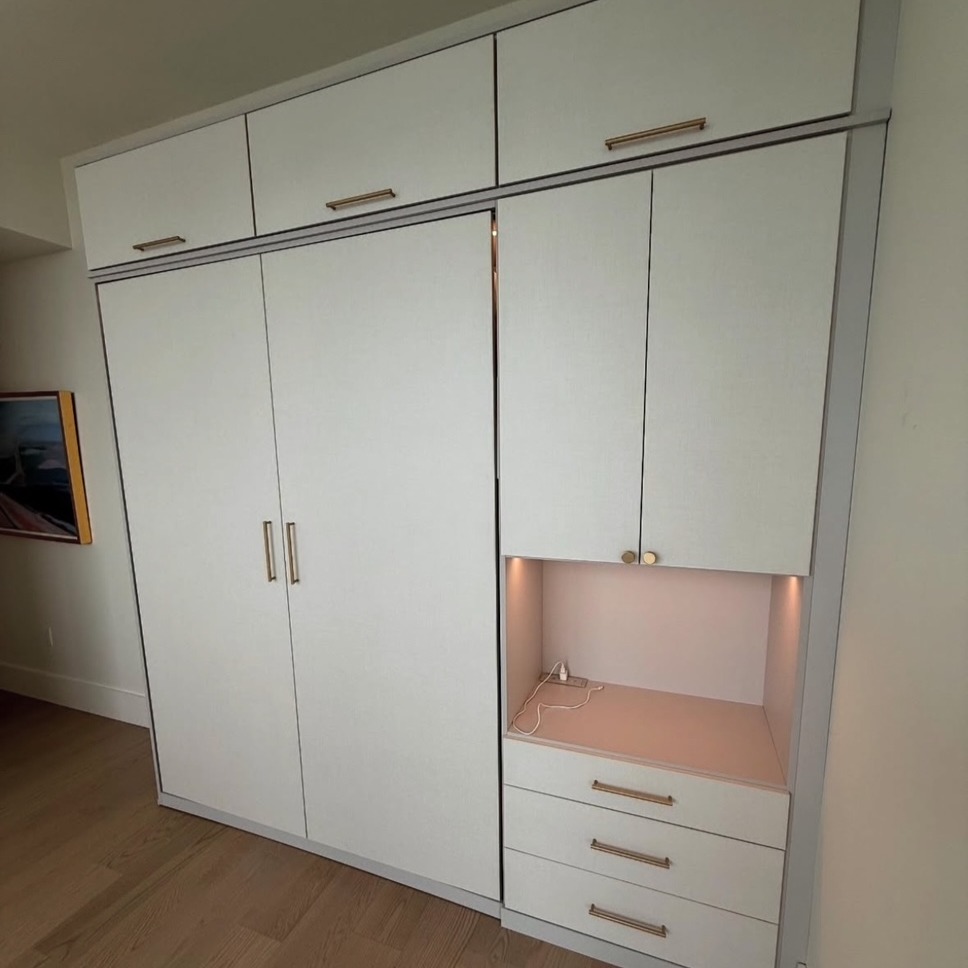 Wall Bed in Sunset Mist with Linen Accents Custom wall bed in Sunset Mist finish with Linen doors and drawer faces, featuring Pub House knurled handles in satin brass, integrated lighting, and a Surface Dean power source for modern convenience.