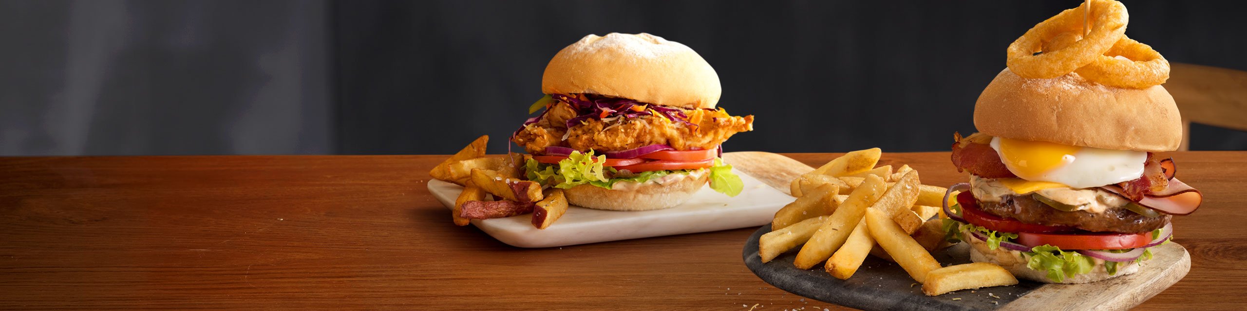 Mugg & Bean Gourmet Burgers – Big Daddy and Buttermilk Chicken with a portion of chips, on a wooden table