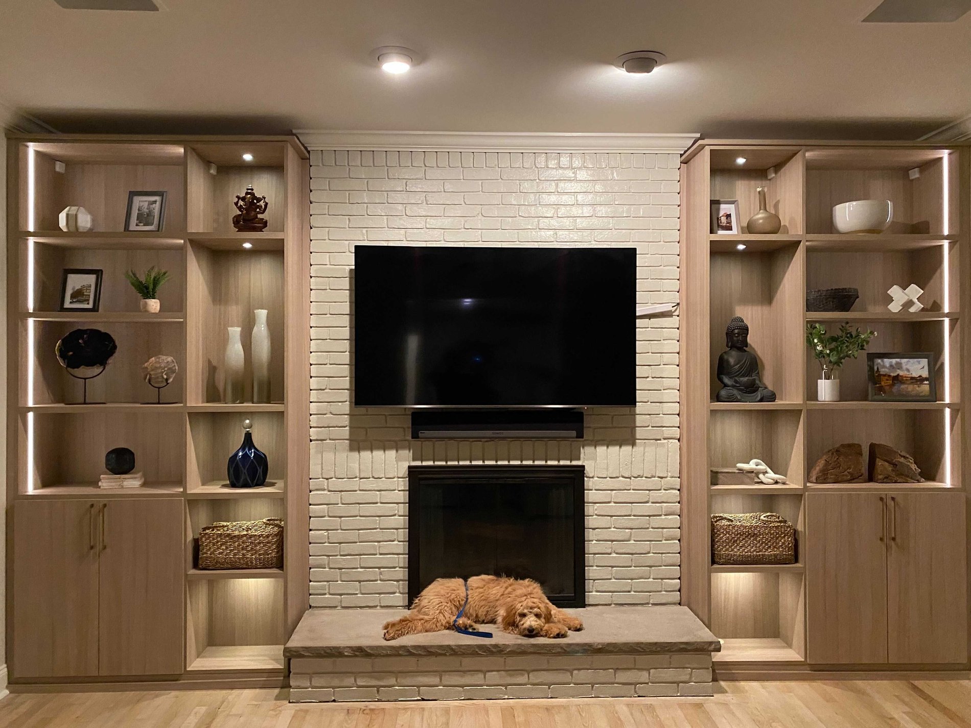 Built-ins Flanking the Fireplace two built-ins in brown with shelves and lower cabinets on each side of a fireplace with TV above and dog
