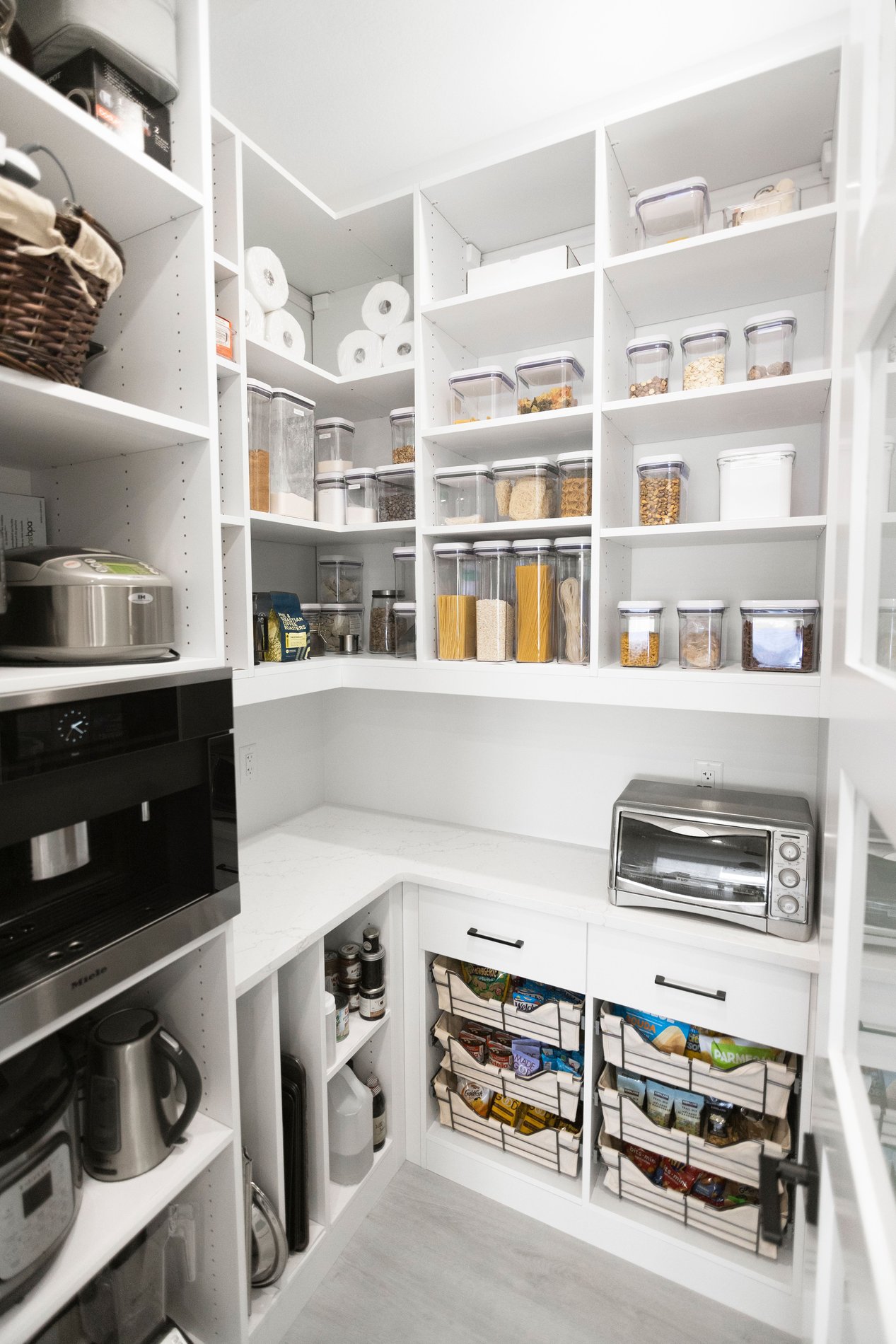 White Pantry California Closets pantry designed in a white finish with a countertop, open shelves, baskets with liners, vertical shelving for cookie sheets.