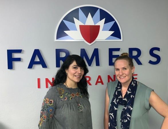 Two women standing by a Farmers logo wall