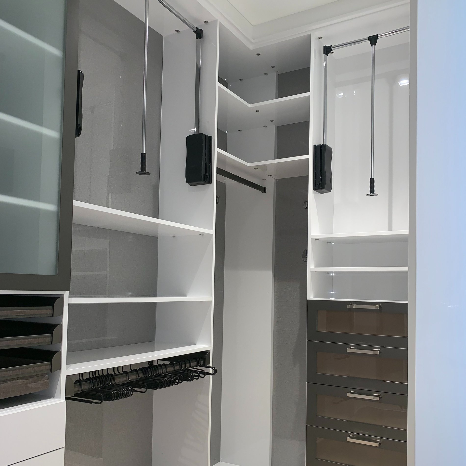Sophisticated Walk-In Closet in Dove with Modern Metal Accents and Smart Storage WALK IN closet in DOVE with BACK PAINTED GLASS BACKING, a WARDROBE LIFT, METAL FRAMED DOORS and GRAPHITE ENGAGE PULLOUTS and PANT RACKS