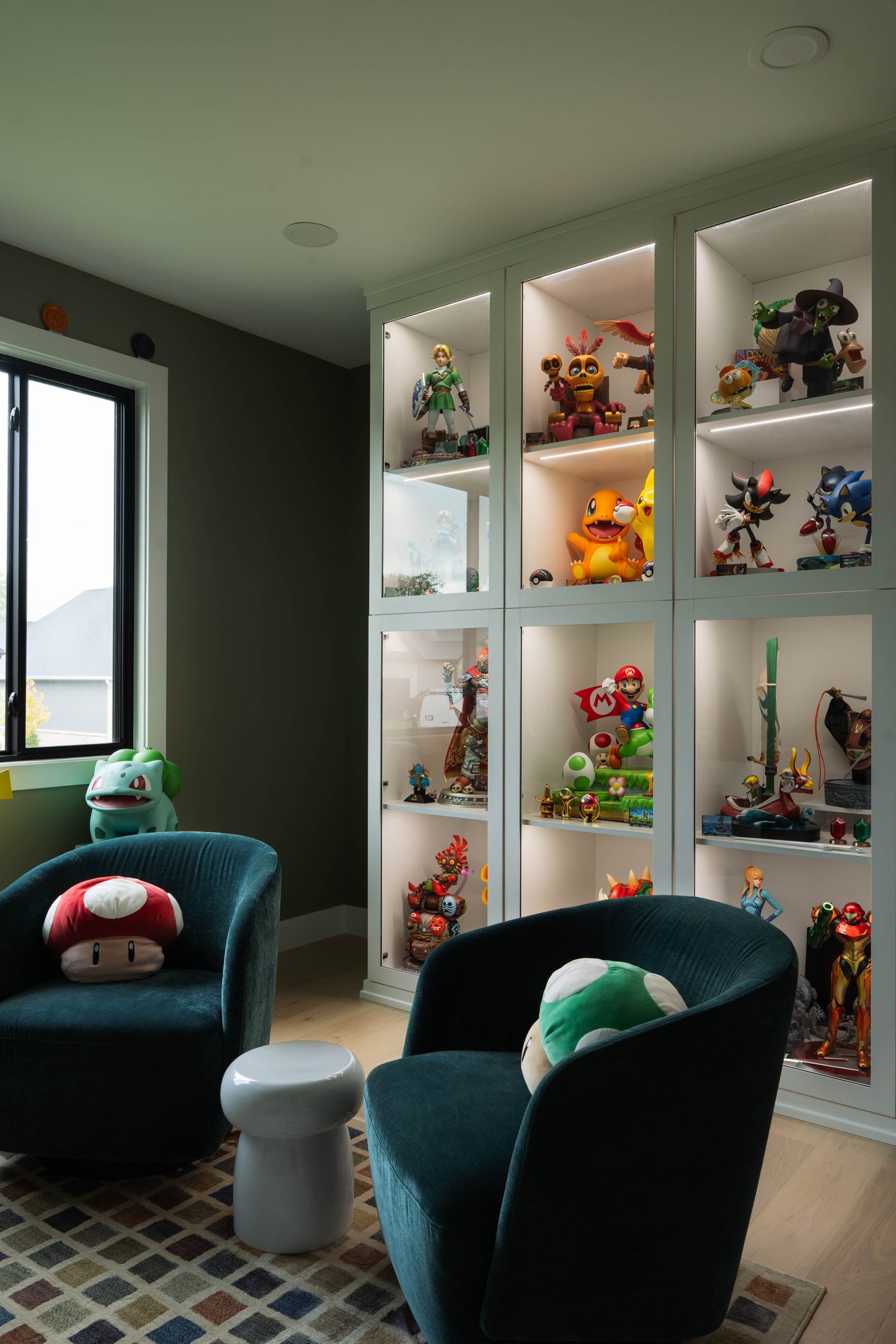 Custom Collectible Display Cabinet with Built-In Lighting Built-in white display cabinet with LED-lit glass shelves showcasing collectible figures and memorabilia in a dedicated game room or lounge space.