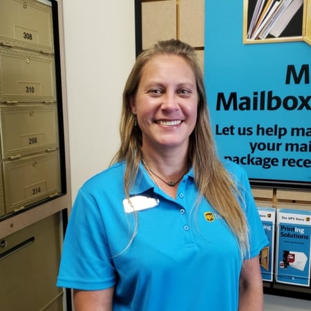 Smiling female associate standing in front of mailboxes in The UPS Store