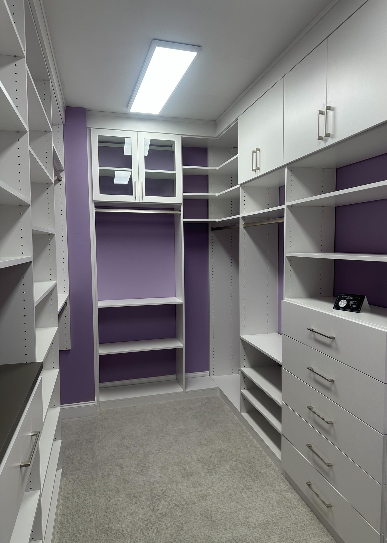 Modern work space with dark framed art Greensboro - Custom closets - purple walk-in closet with white shelving, drawers, cabinets, and a glass cabinet for display items