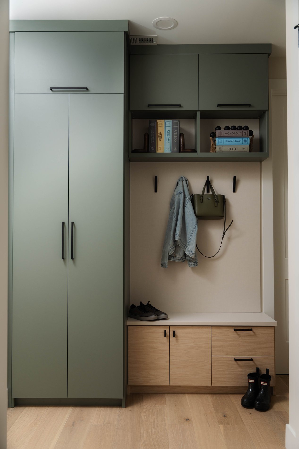 Custom Mudroom Storage Bench with Hooks, Drawers & Open Shelving Custom entryway mudroom with storage bench, cabinet doors, drawers, wall hooks holding a jacket and handbag, overhead shelves, and footwear storage.