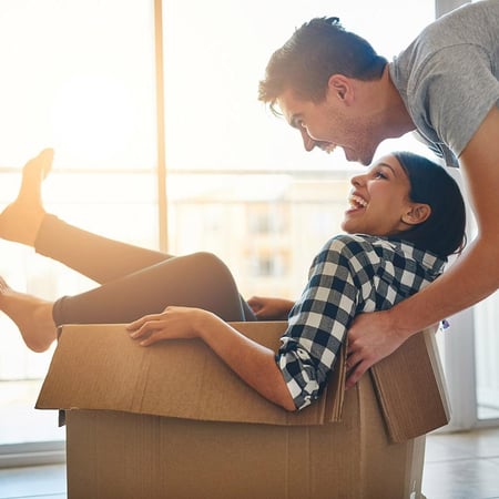 Woman in packing box being pushed by man around home