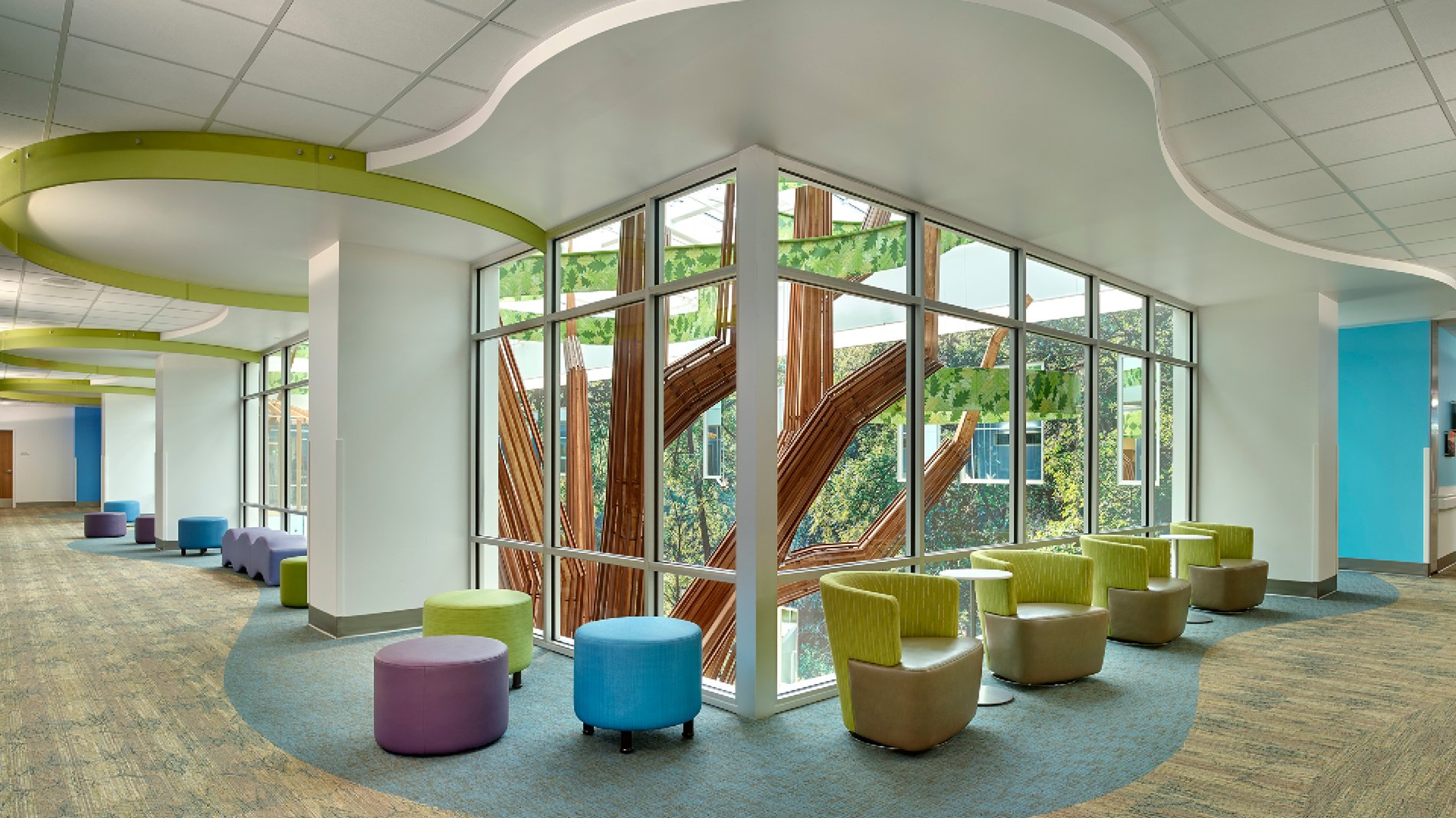 Inside a hallway in Beacon Children's Hospital, with colorful furniture and a view of the playful tree sculpture in the atrium.