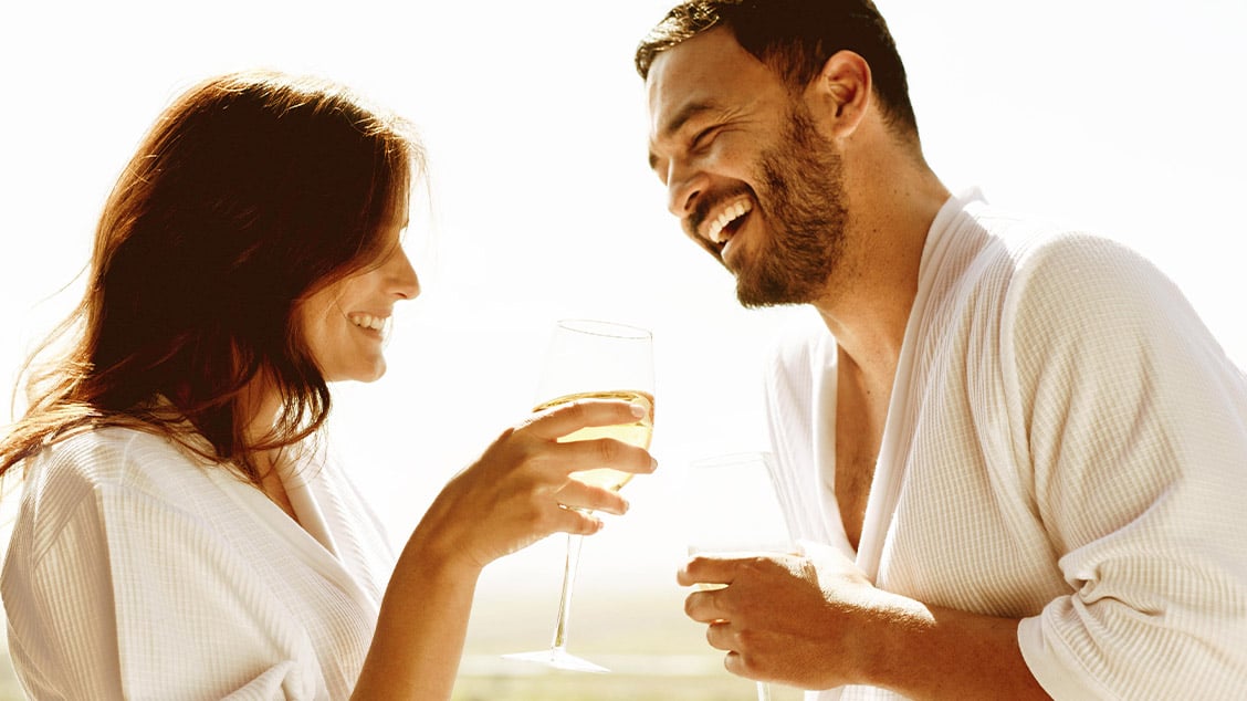 Man and women in bathrobe drinking white wine.