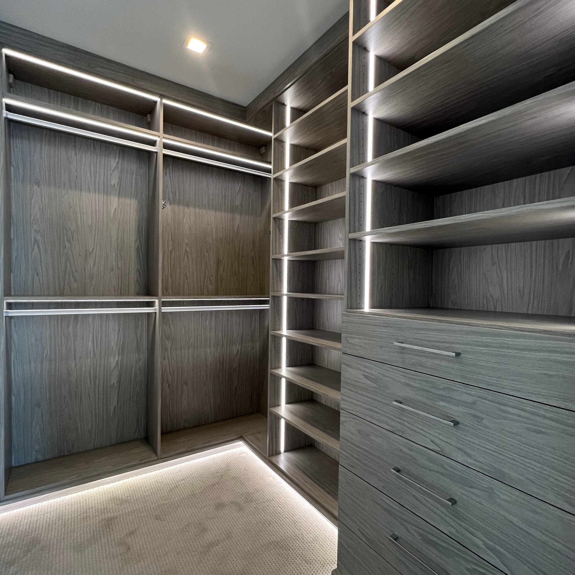 Contemporary Walk-In Closet in Grigio with Sleek Lighting and Slab Drawers WALK IN closet in GRIGIO with BACKING, a RECESSED TOE KICK LIGHTING and VERTICAL STRIP LIGHTING with SLAB DRAWERS