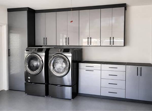 Custom garage storage with high-gloss cabinets, built-in laundry room cabinets, washer and dryer, drawers, and countertop workspace by California Closets in Boca Raton, Florida. Custom garage cabinets with high-gloss doors, built-in laundry room storage, washer and dryer, drawers, and countertop by California Closets in Boca Raton, FL.