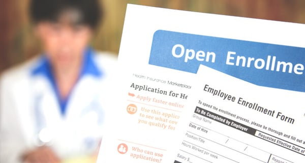 A person holds up employee enrollment forms and a nurse appears in the background