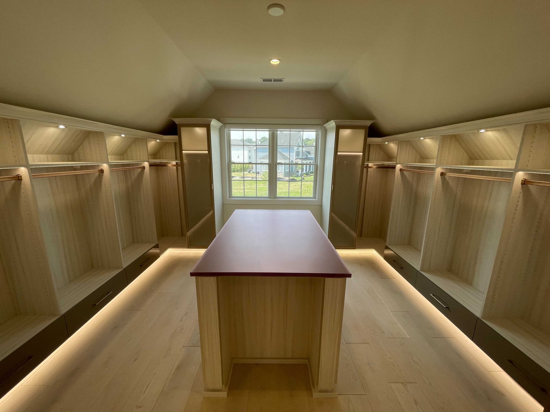 Truly a Custom Closet closet with sloped ceiling, hanging space and lighting, center island in light wood color