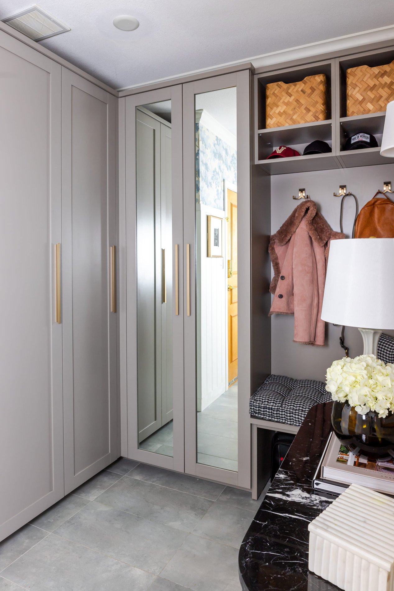 Grey mudroom with gold accents Mudroom with small built in bench and mirror door fronts on a two door cabinet