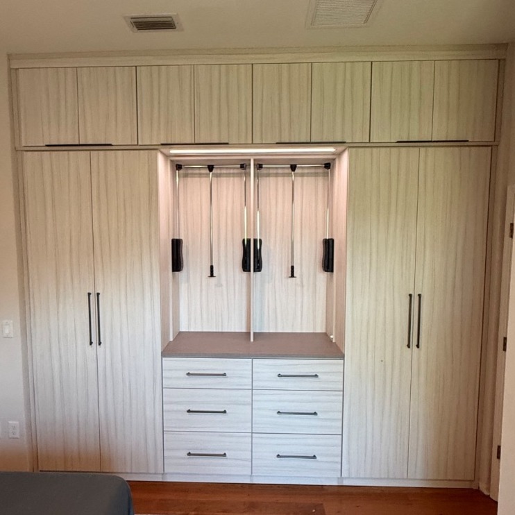 Custom master bedroom wardrobe in Tuscan Moon with graphite hardware, featuring two pull-down rods for easy garment access and LED strip lighting inside and along the center exterior.