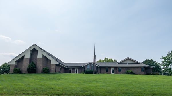The Church of Jesus Christ of Latter-day Saints meetinghouse in Athens, Tennessee, as viewed from Cedar Springs Road. The viewer is presented with a brown brick building with a large pitched roof on one end, smaller pitched roof on the opposite end. Three metal ornamental spires are positioned on a green grass landscape, immediately in front of and centered to the meetinghouse. The name "The Church of Jesus Christ of Latter-day Saints" is mounted on the meetinghouse brick.