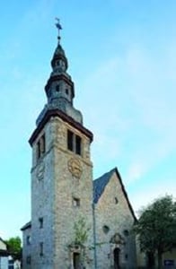 Außenansicht der Kirche vor blauem Himmel. Auffällig ist der hohe Kirchturm.