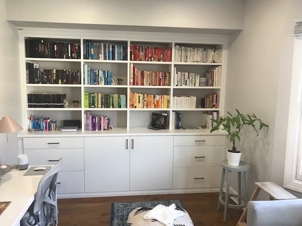 white built-in bookshelves with lower cabinets and books organized by color