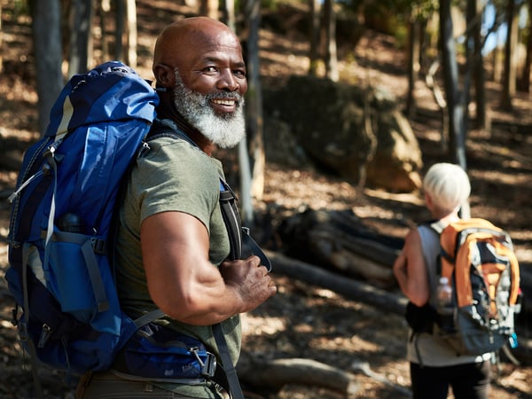 smiling bearded man wearing backpack while hiking with wife