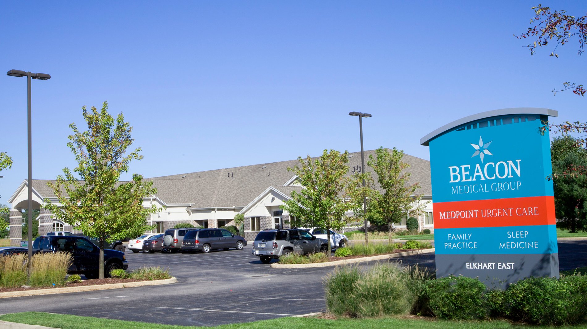 A teal sign stands in front of the parking lot for Beacon Medical Group Elkhart East