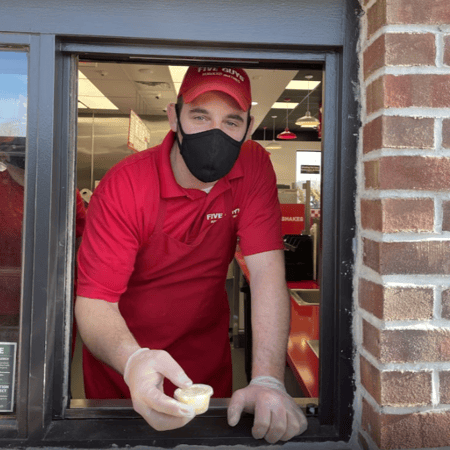 A Five Guys employee hands a souffle cup to a customer via mobile pickup window.