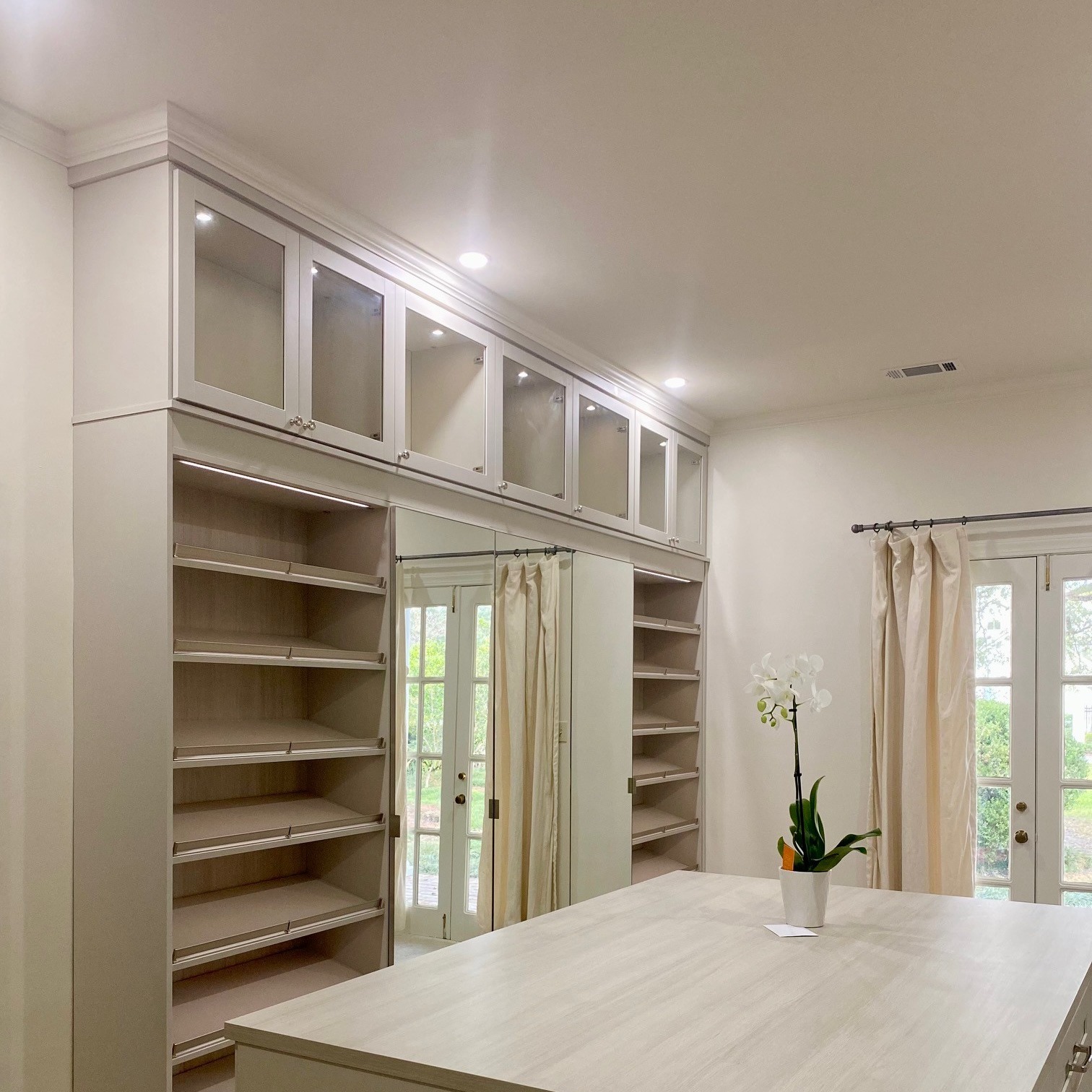 Light gray walk-in closet organization with island and shoe shelving by California Closets Baton Rouge, Louisiana.