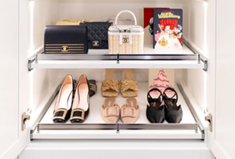 a custom walk-in closet with integrated lighting and pull-out shoe storage shelves by California Closets