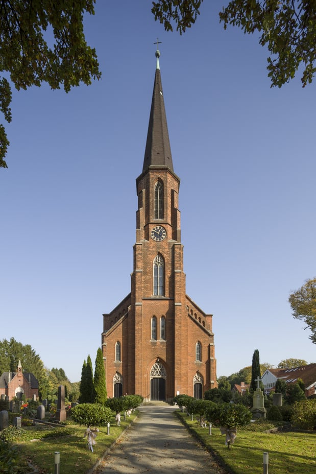 Das Kirchengebäude aus Backstein umgeben von einem Friedhof.